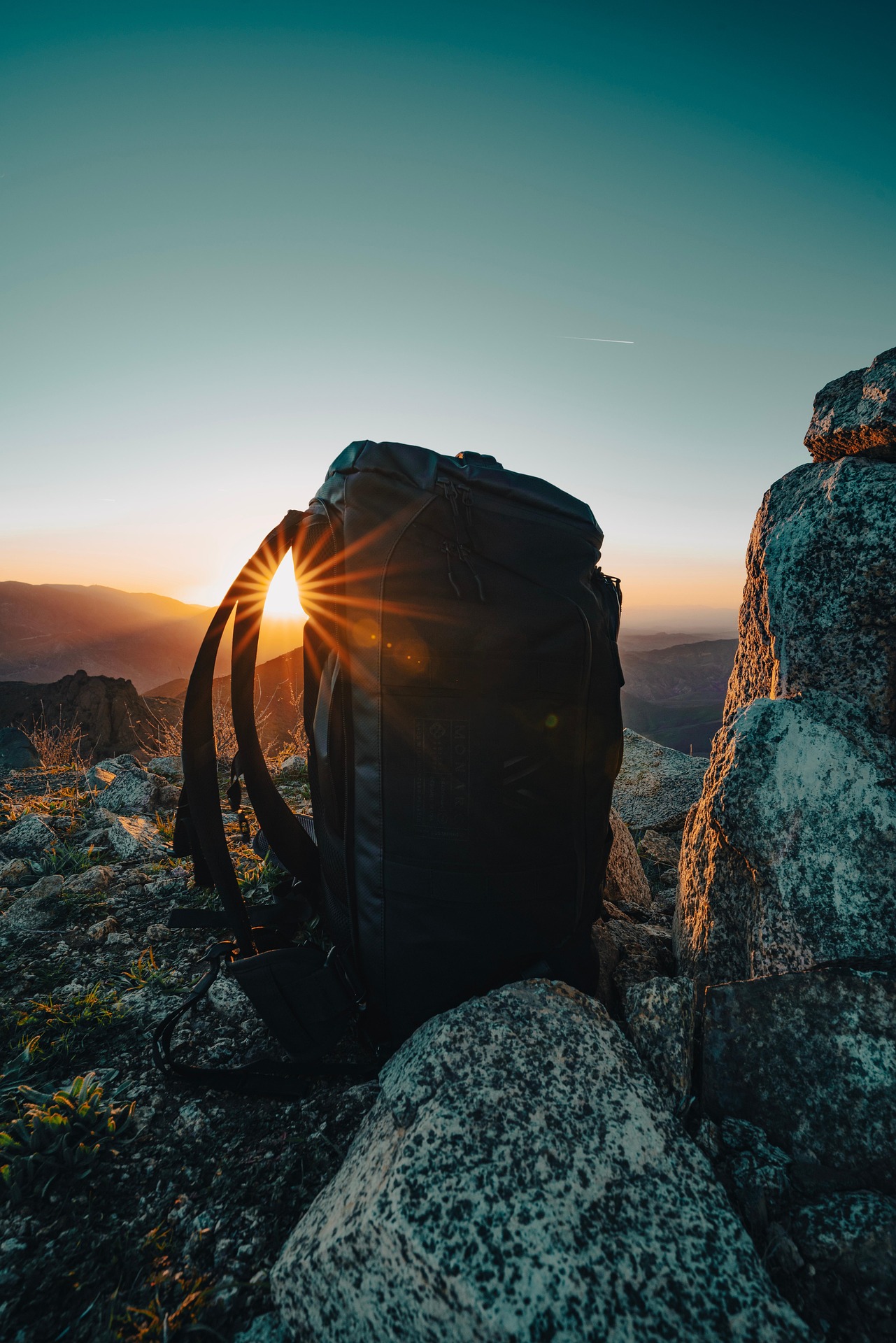A loaded backpack sits on a rocky ridge silhouetted against a setting sun