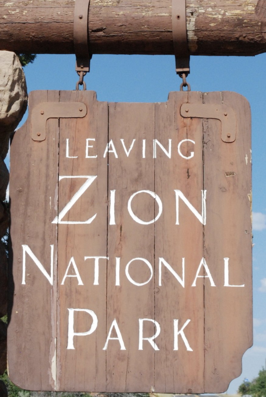 Weathered wooden sign reading Leaving Zion National Park hanging from a log crossbeam
