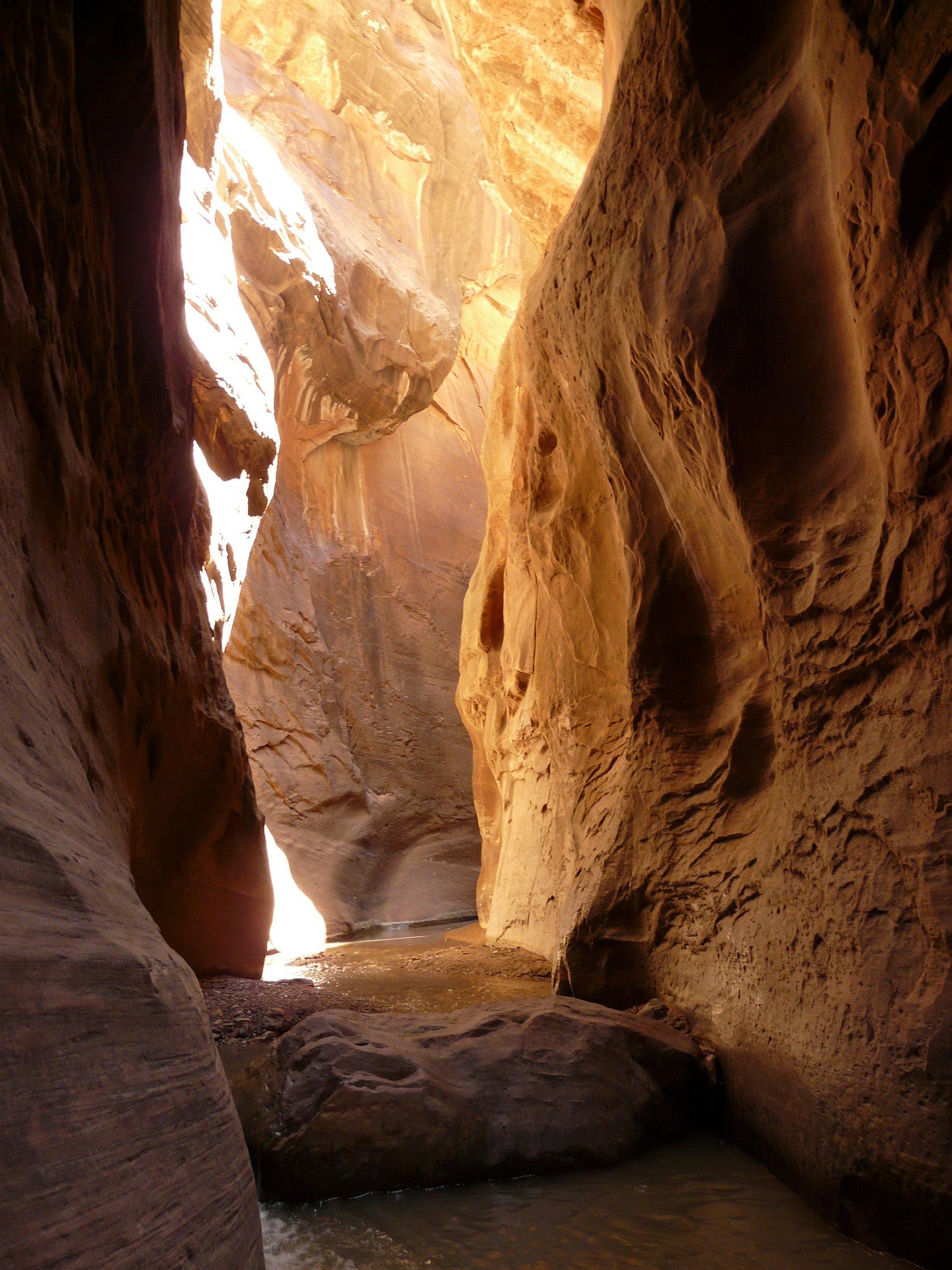 Reflected golden light on the walls of a narrow water filled canyon with a boulder in the foreground