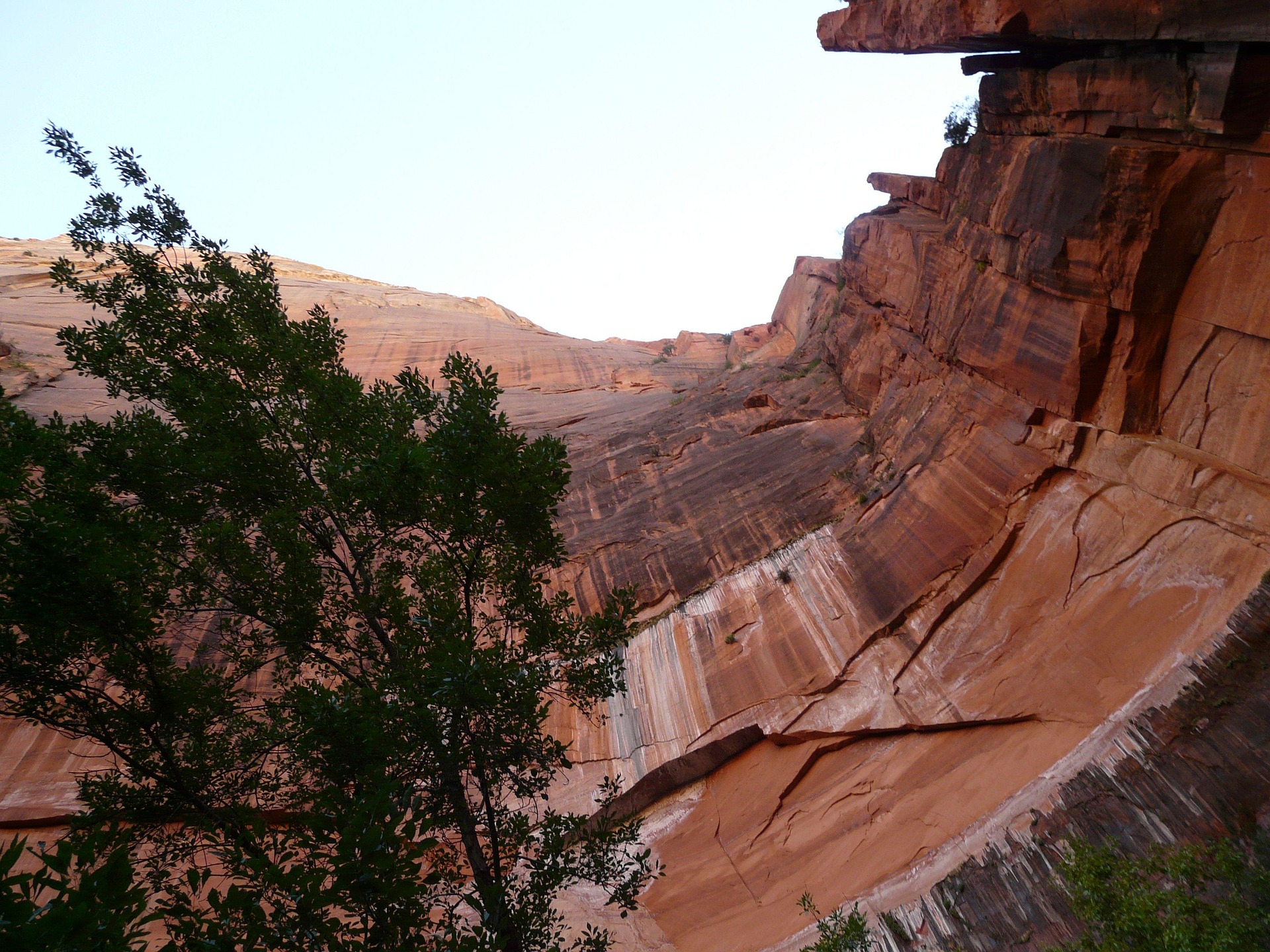 A curving sandstone canyon wall streaked with dark desert varnish, seen from below