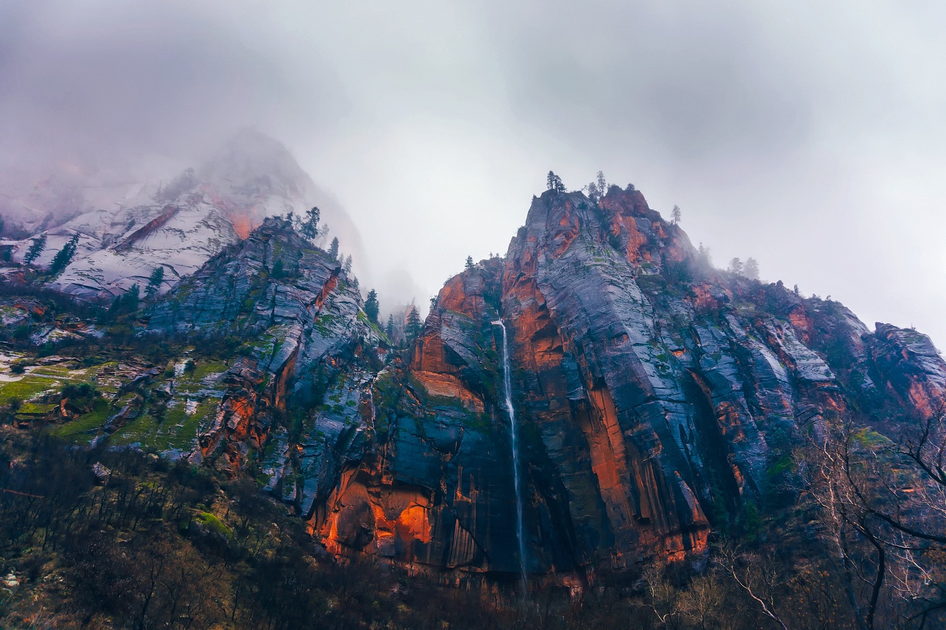 Thin waterfall spilling from a snow dusted cliff in Zion Canyon with fog hanging along the rim