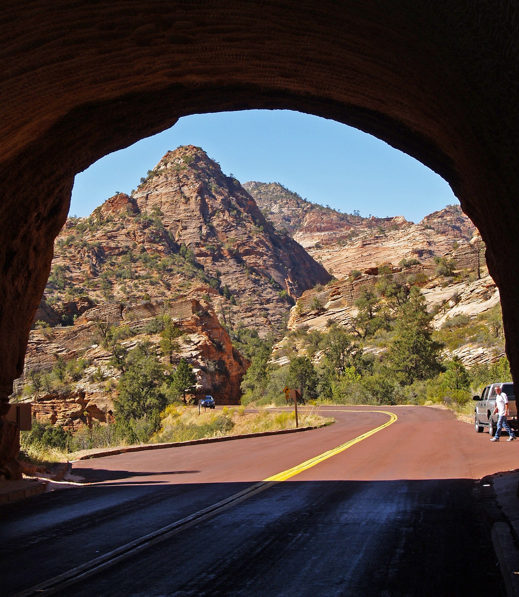 View out of a tunnel portal on the Zion Mount Carmel Highway toward red rock peaks and the red asphalt road