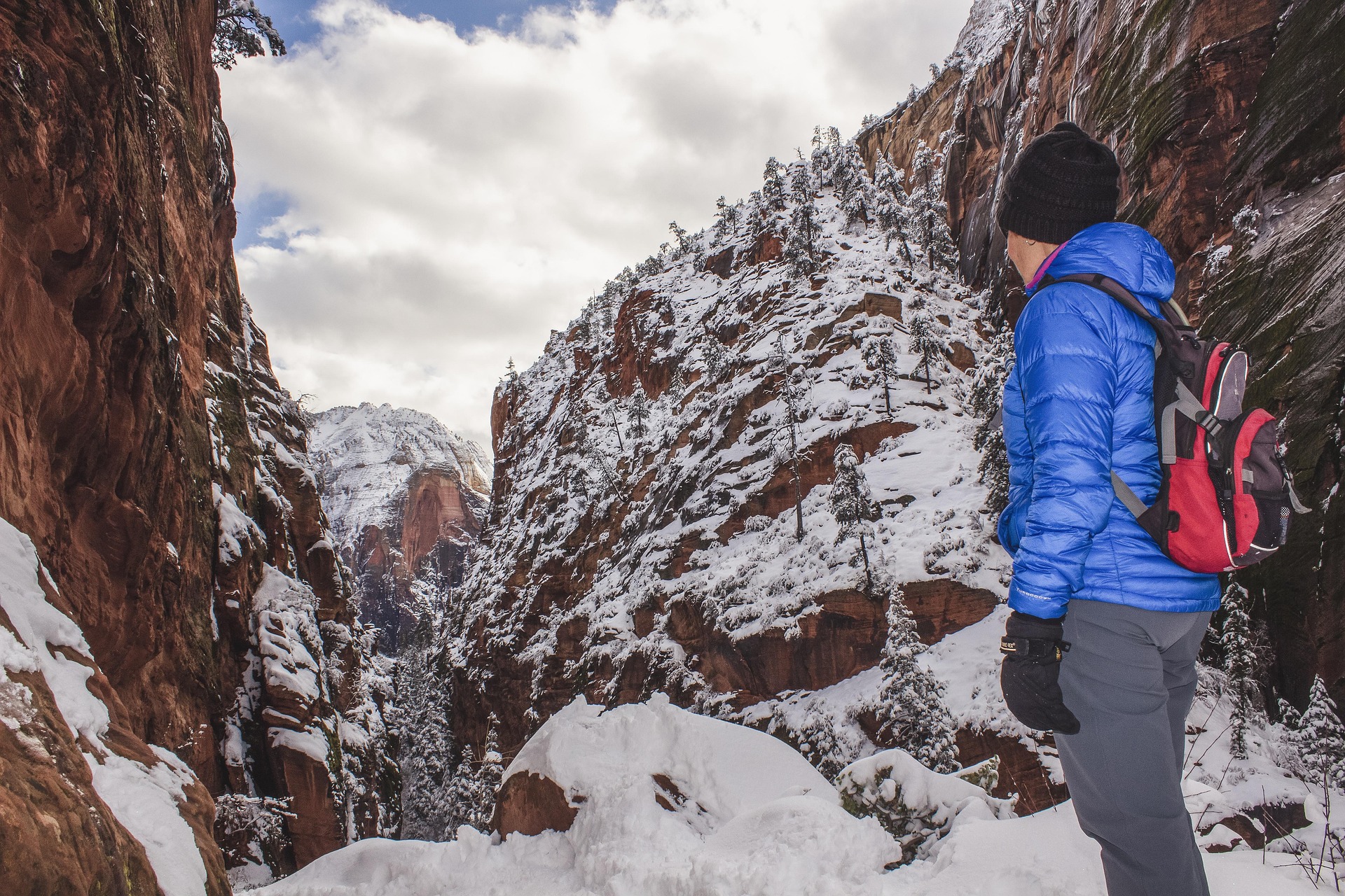 Hiker in a blue down jacket pausing on a snow covered trail between sandstone walls in Zion